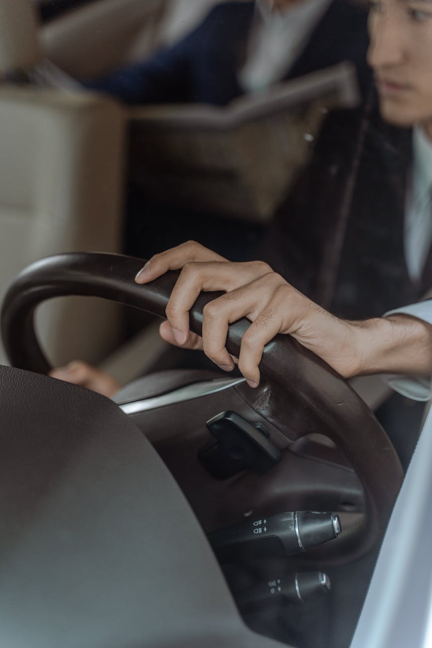 Close-up shot of a chauffeur's hand on the steering wheel, driving a luxury car interior.